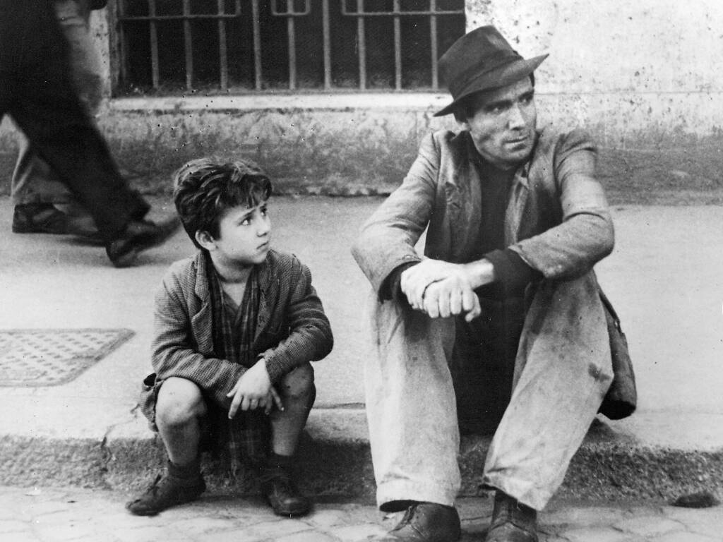 A father and son sit in despair on the streets of post-war Rome in a scene from Bicycle Thieves